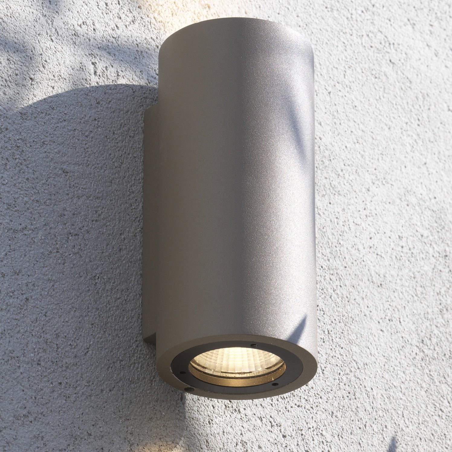 Cylindrical outdoor wall light fixture on a textured white wall